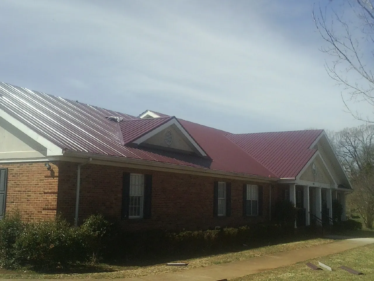 Red metal roof with gabled entries on a long brick building, from a Hail Damage Roof Repair job in Tipp City