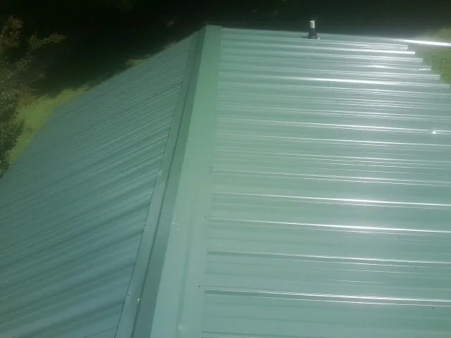 New green metal panels meeting at the ridge of a roof — Flat Roof Repair work by our crew in Tipp City