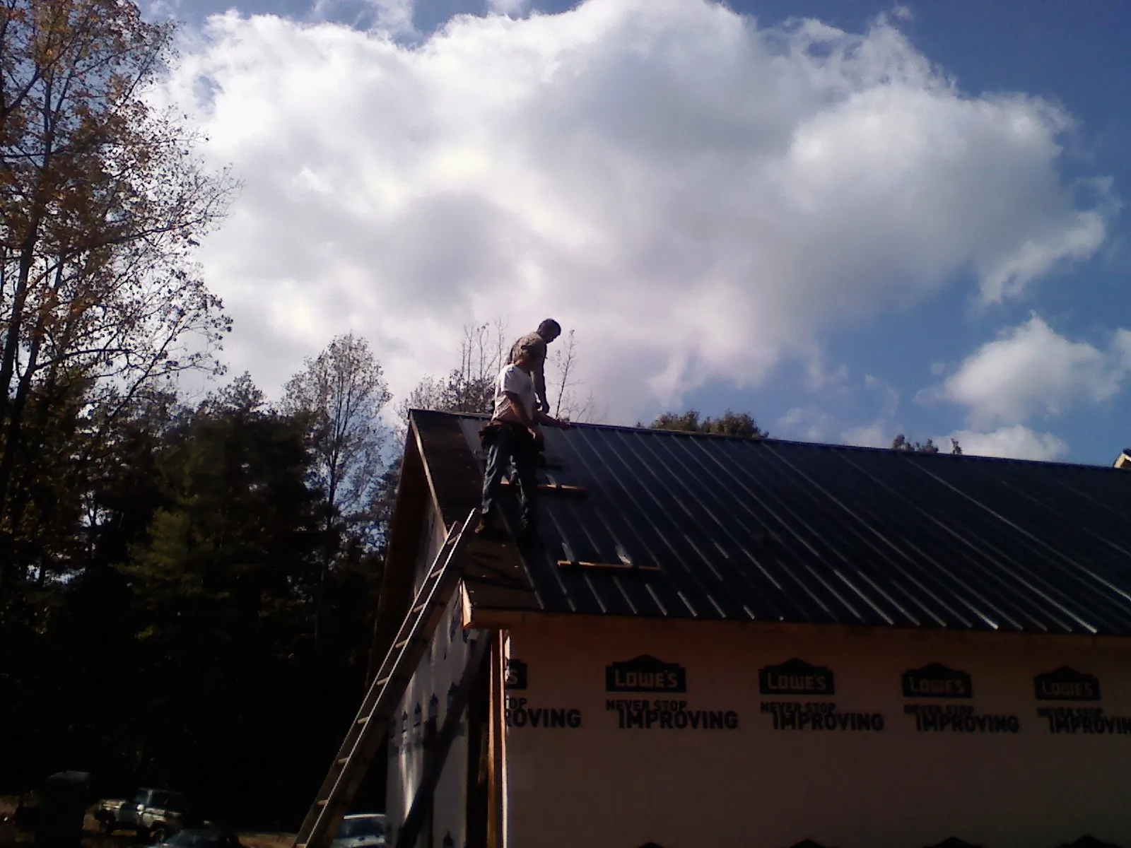 Roofer fastening dark metal panels high against a cloudy sky, from a Roof Inspection job in Tipp City