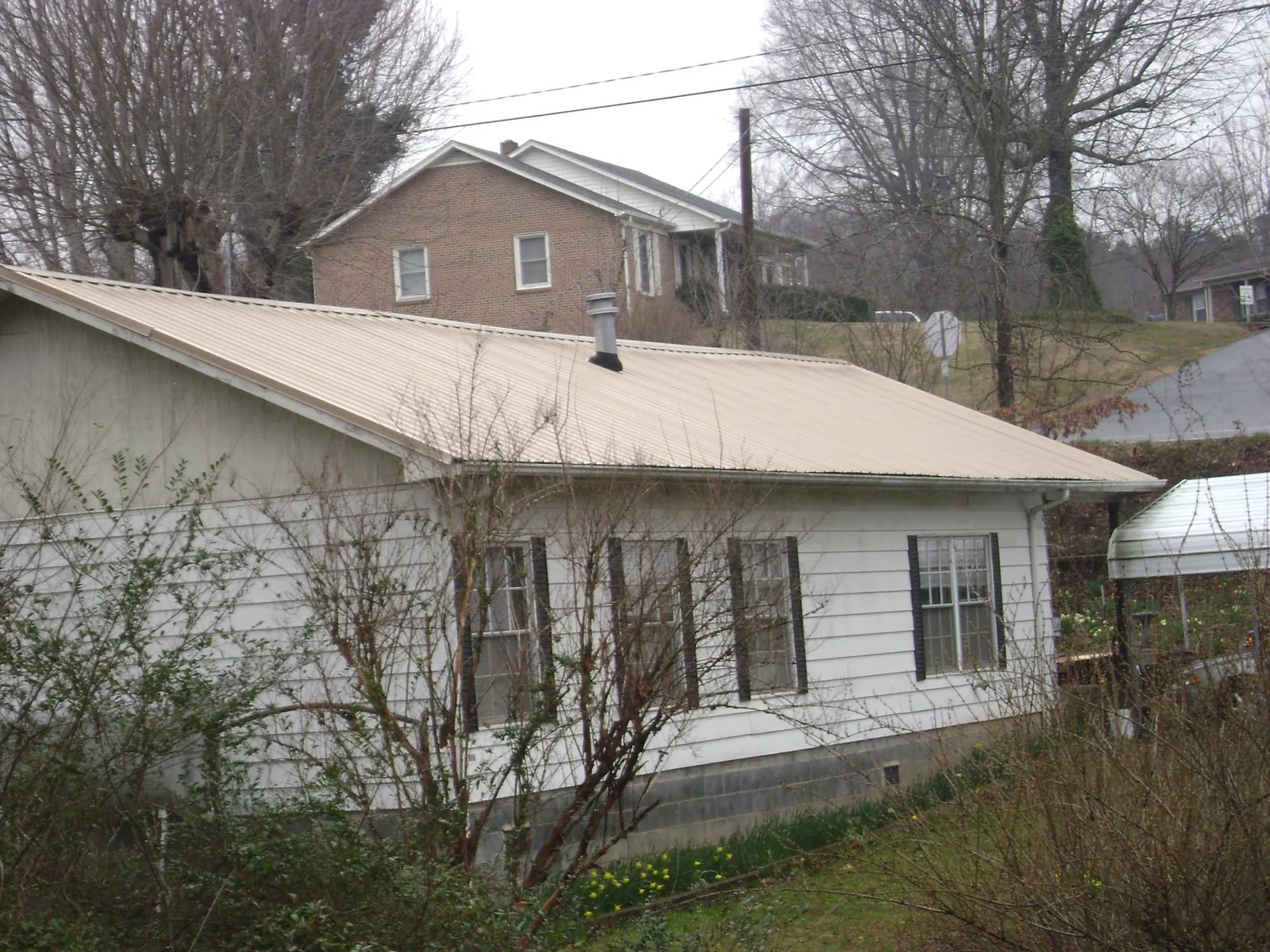 Tan metal roof on a white sided house set into a hillside — Commercial Roofing by Roofing Brothers in Tipp City